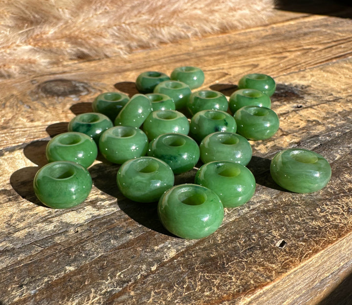Cluster of jade donut beads with holes scattered on a rustic wooden surface