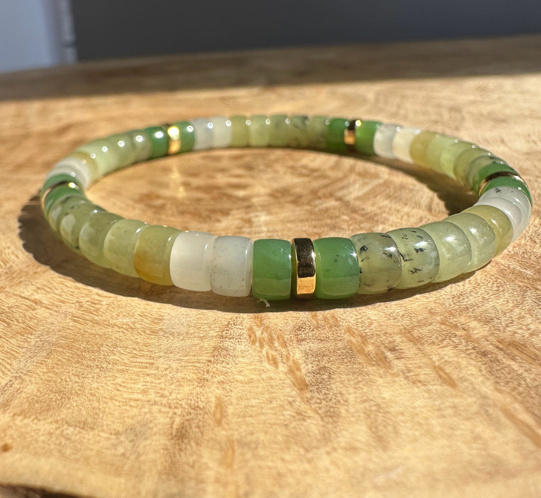 Natural nephrite jade bracelet with green and pale white rondelle beads coiled on a wood surface.