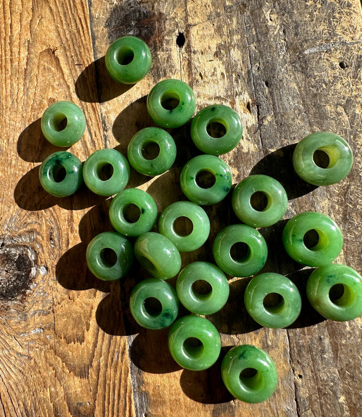 Top down view of numerous green jade beads with holes on a weathered wooden surface