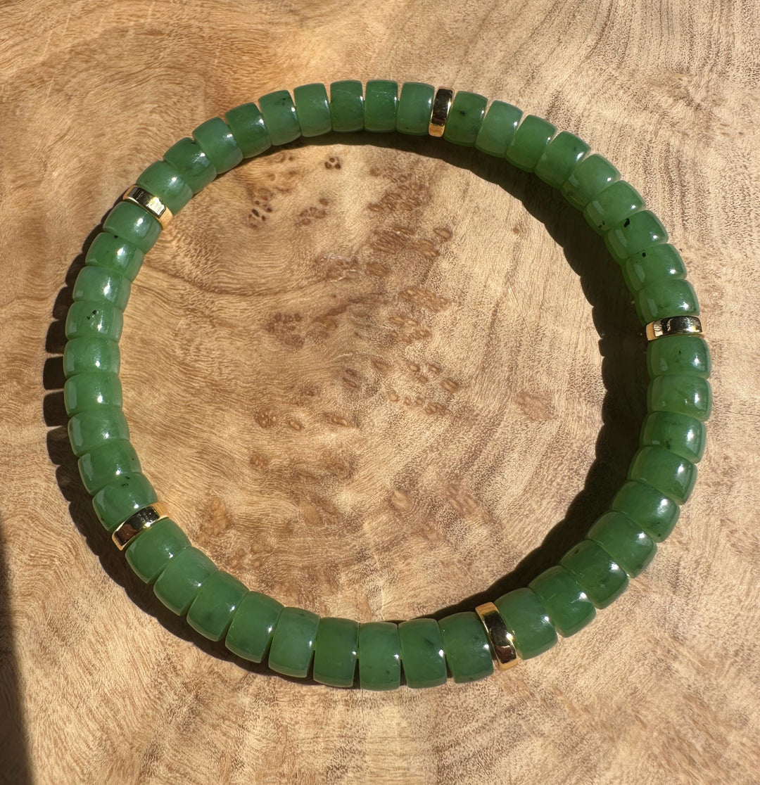 Curved Canadian nephrite jade bead bracelet with gold spacers on a wooden surface.