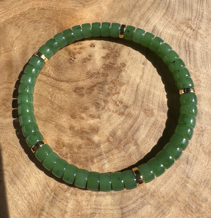 Curved Canadian nephrite jade bead bracelet with gold spacers on a wooden surface.