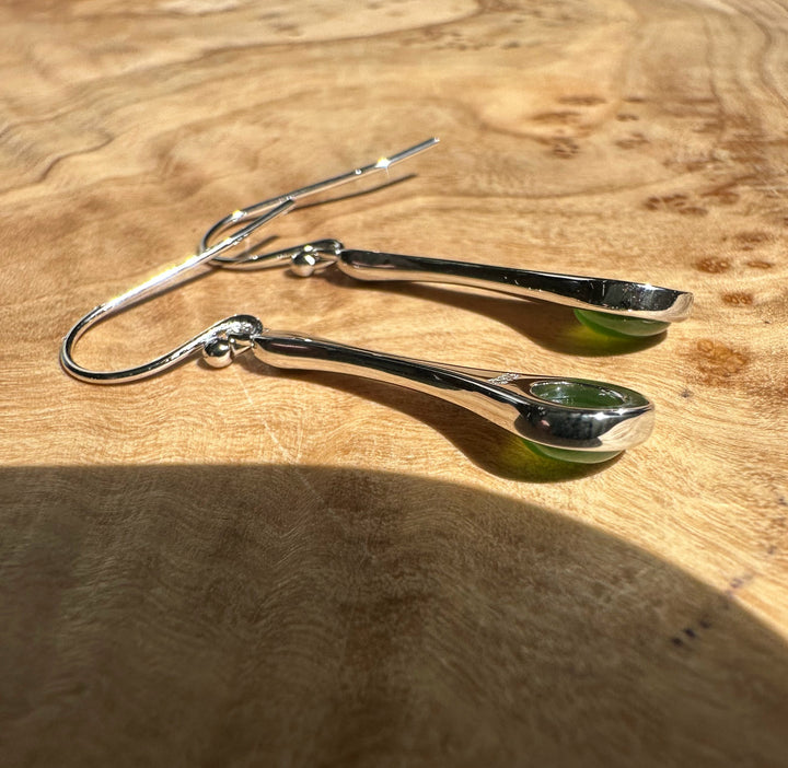 Silver drop earrings with curved tapered bars and green cabochons resting on wood