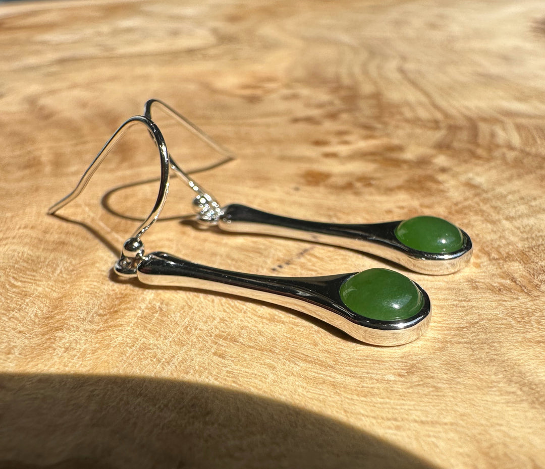 Silver drop earrings with green cabochon stones laid on a warm wooden surface.