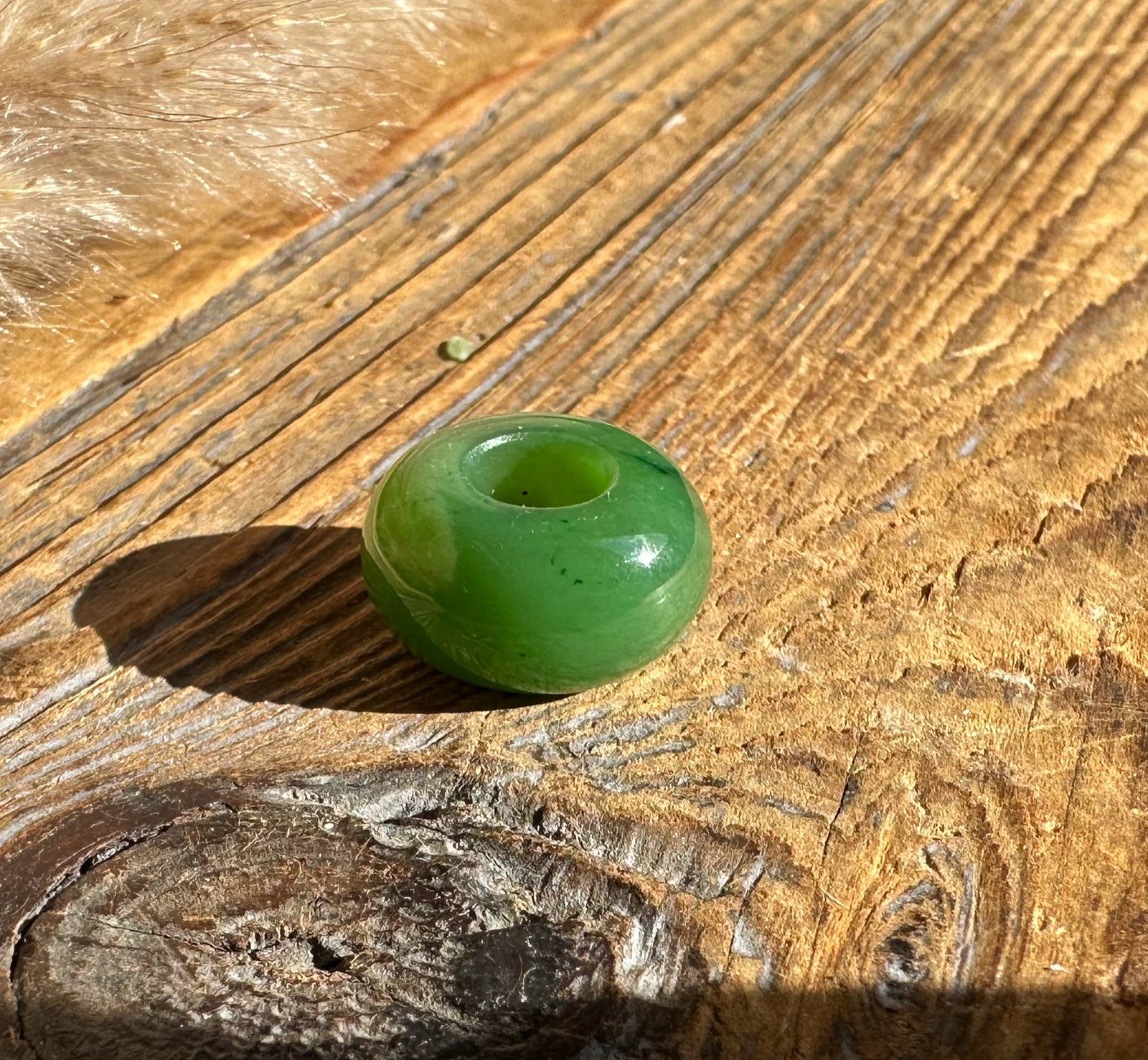Single glossy jade bead with a central hole on sunlit wood