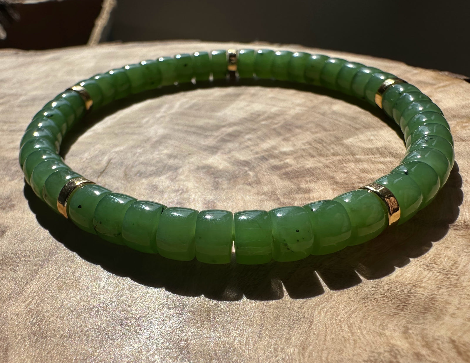 Close-up of green nephrite jade bead bracelet on a wooden surface with gold spacer beads.