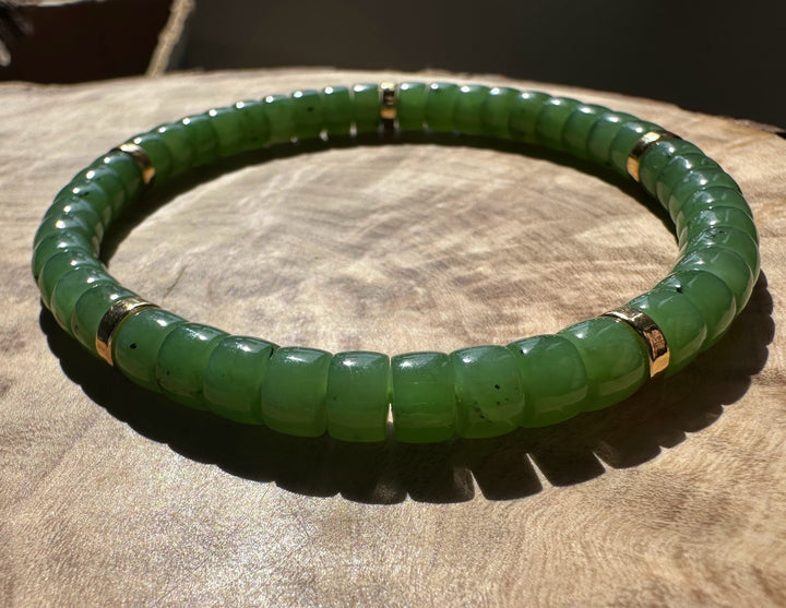 Close-up of green nephrite jade bead bracelet on a wooden surface with gold spacer beads.