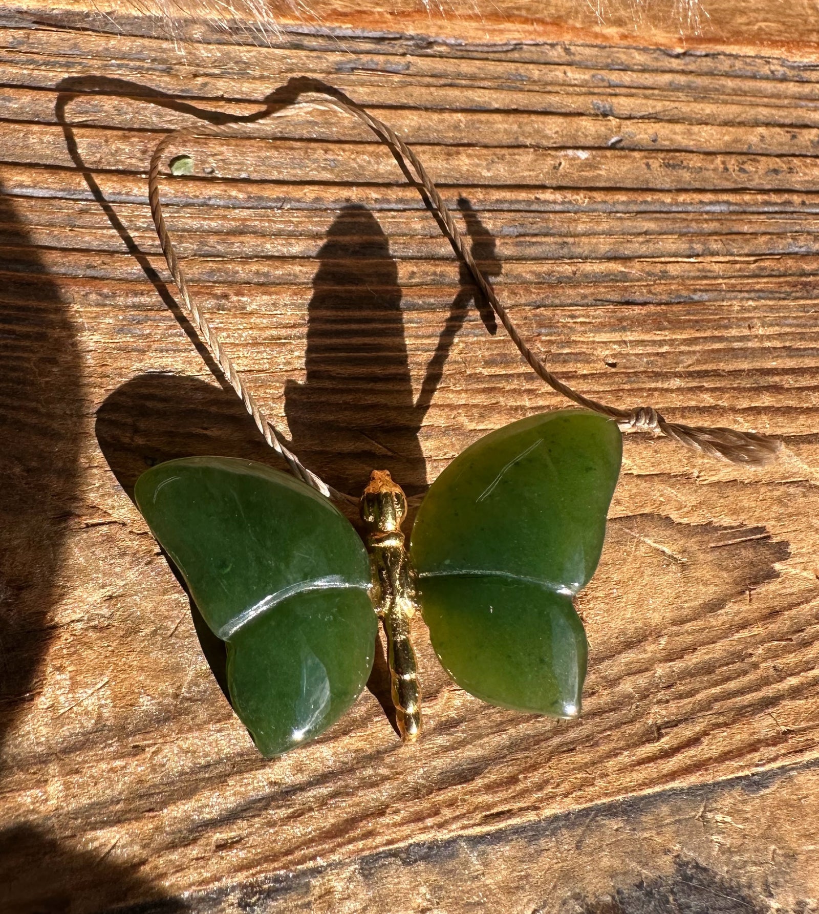 Dark green butterfly pendant with a gold-toned body on a brown cord necklace