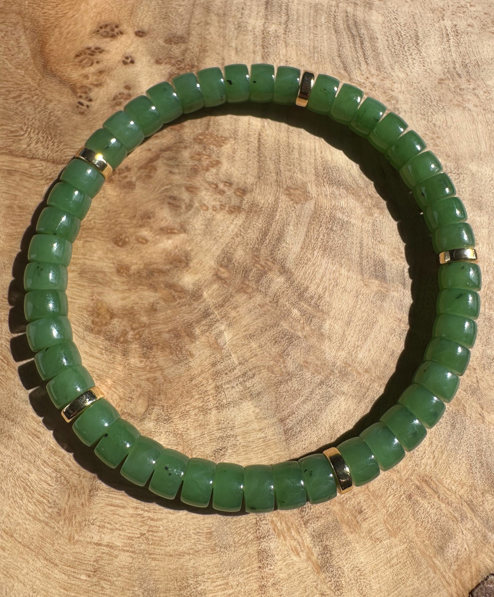 A plus Canadian nephrite jade bead bracelet from King Mountain Mine with uniform green beads and gold spacers on a wood surface.