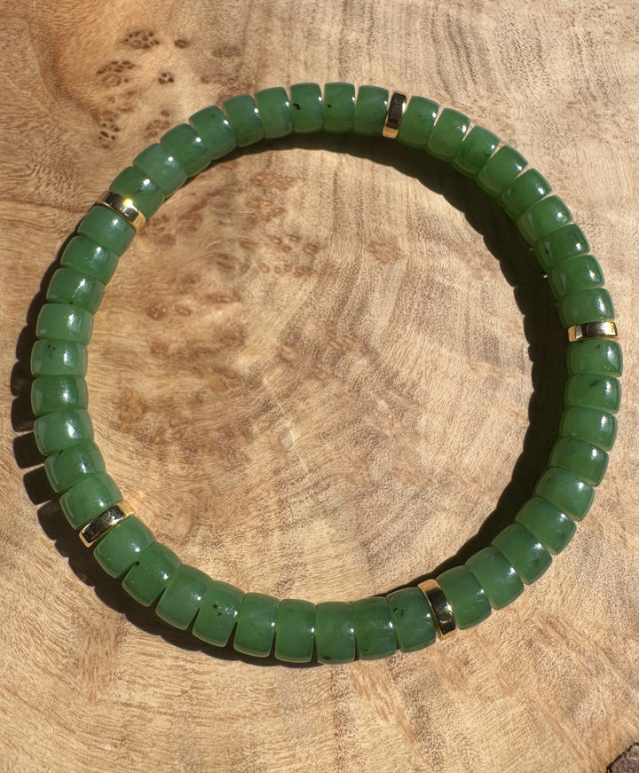 A plus Canadian nephrite jade bead bracelet from King Mountain Mine with uniform green beads and gold spacers on a wood surface.
