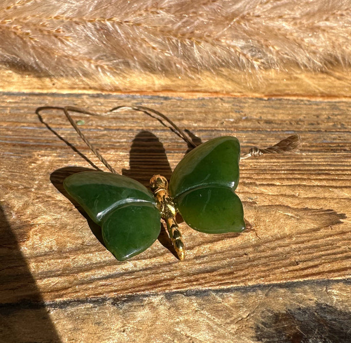Dark green butterfly pendant with a gold body on a cord resting on rustic wood.