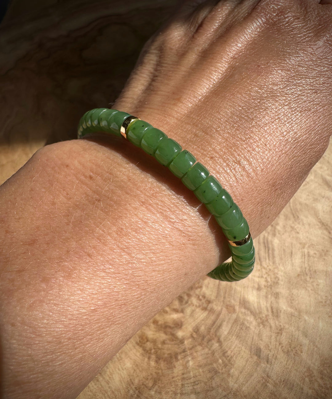 Wrist wearing green nephrite jade bead bracelet with gold spacers.