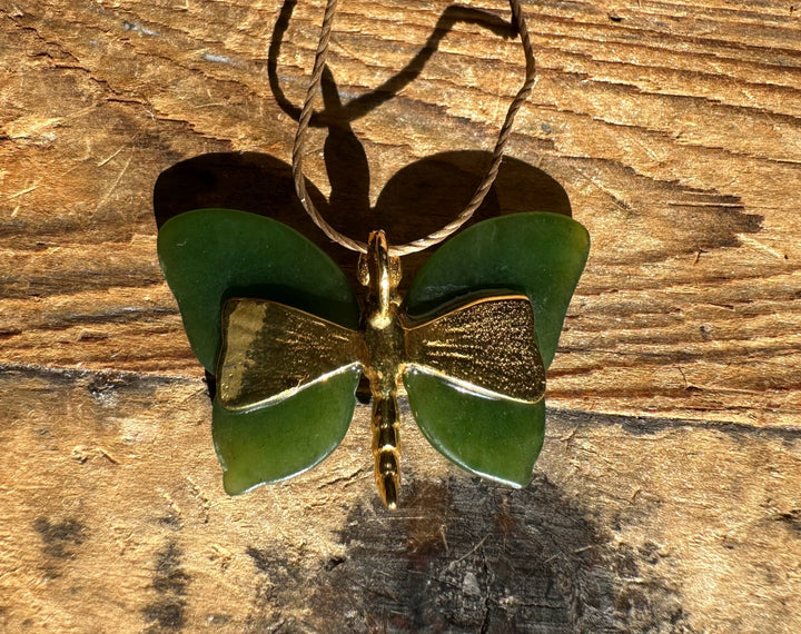 Green butterfly pendant with a gold body and braided cord on a weathered wooden surface.