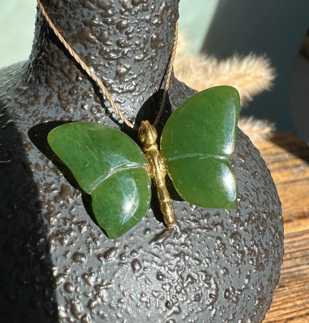 Dark green butterfly pendant with a gold-toned body resting on a textured dark surface