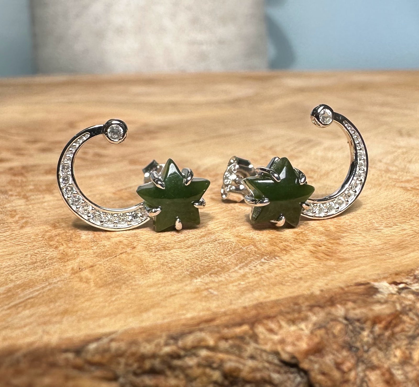 Pair of silver crescent moon stud earrings adorned with crystals and green star accents on a wooden surface