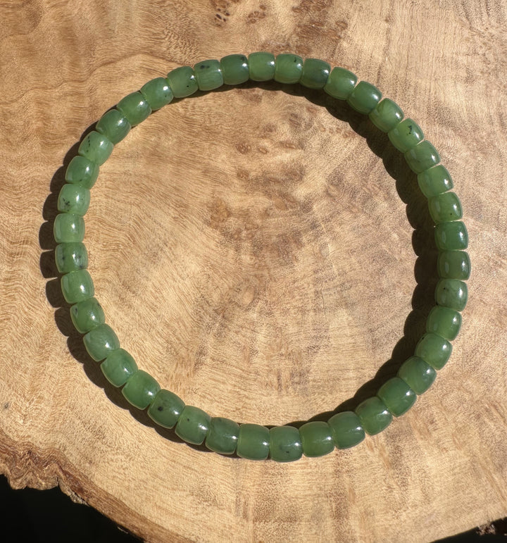 Canadian nephrite jade bead bracelet with rounded green beads and small dark inclusions on a wooden surface.