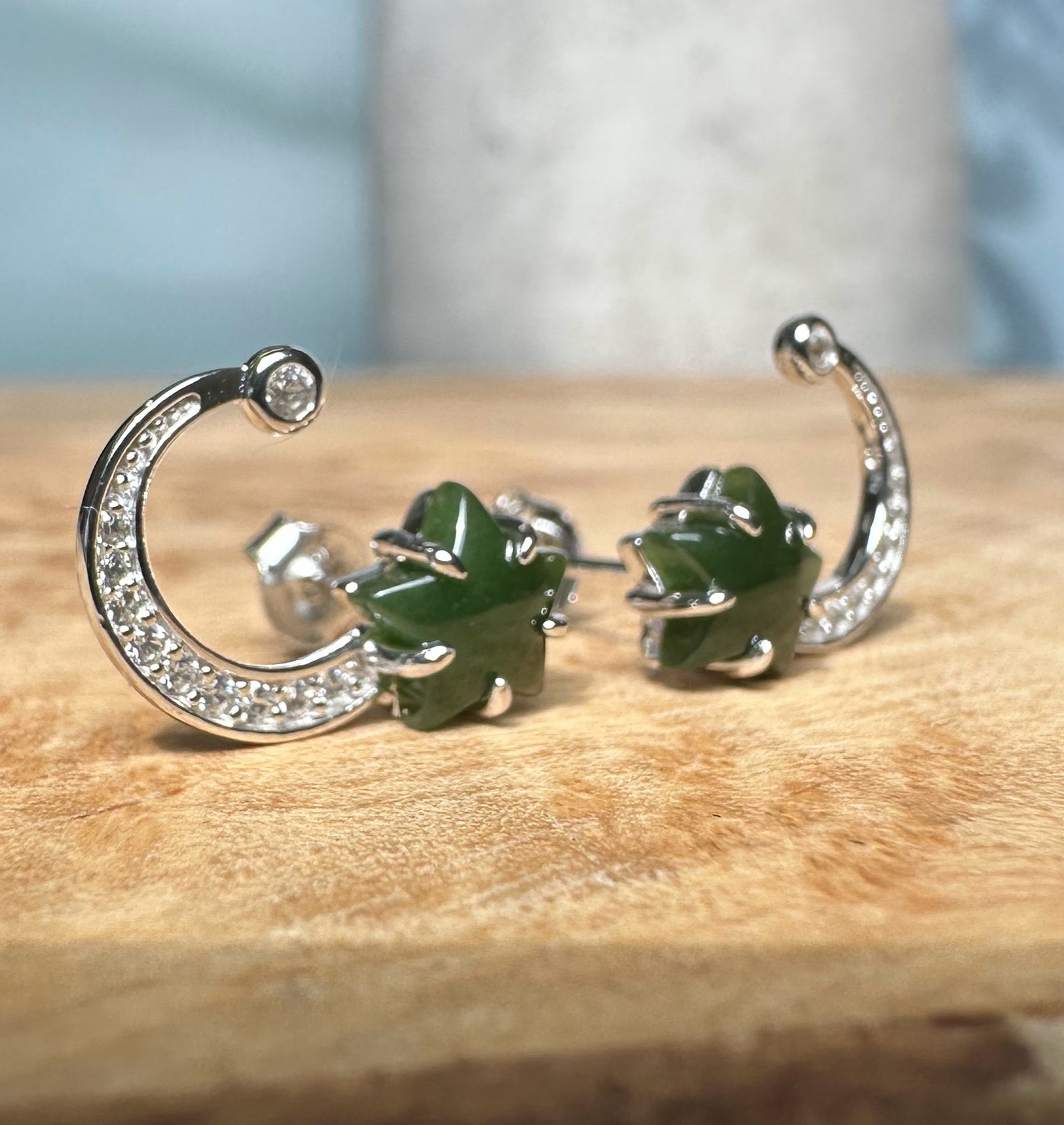 Close up of silver crescent moon earrings with crystal pavé and a green star setting on each end