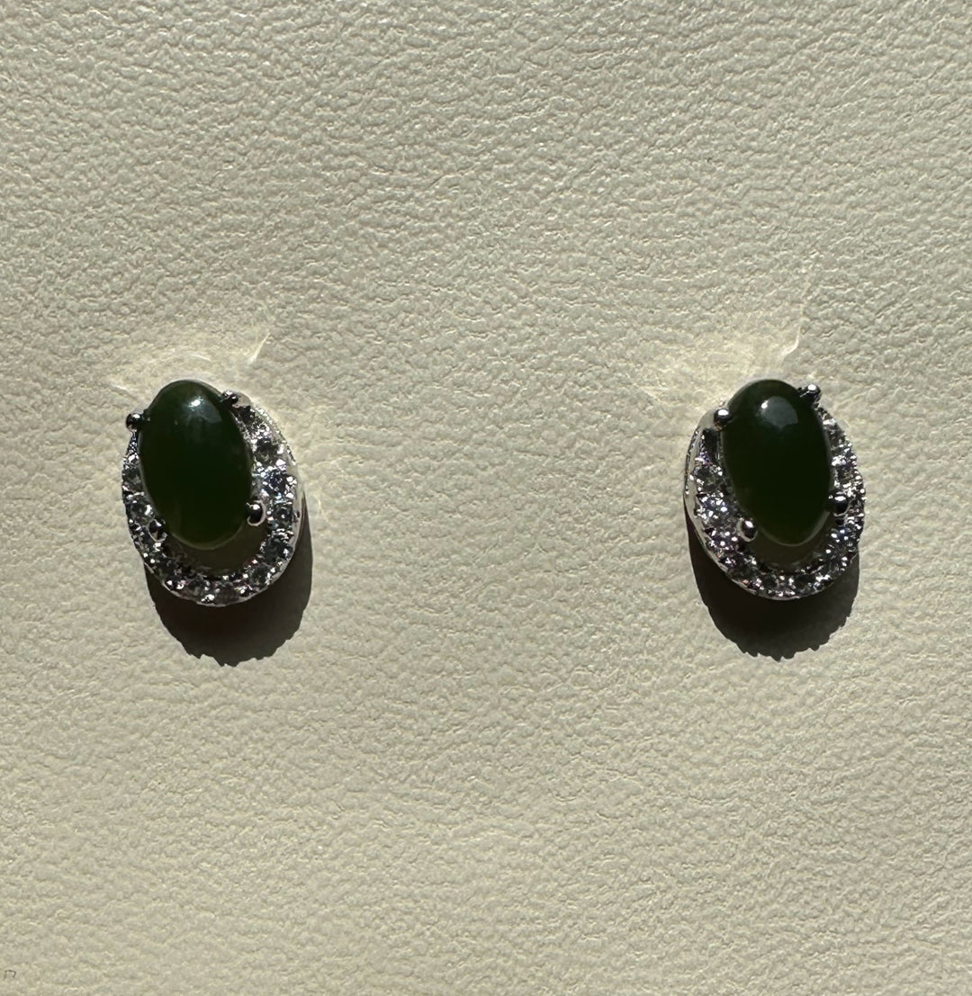 Front view of Silver Jade Studs with green oval jade centers encircled by diamonds on a textured light surface