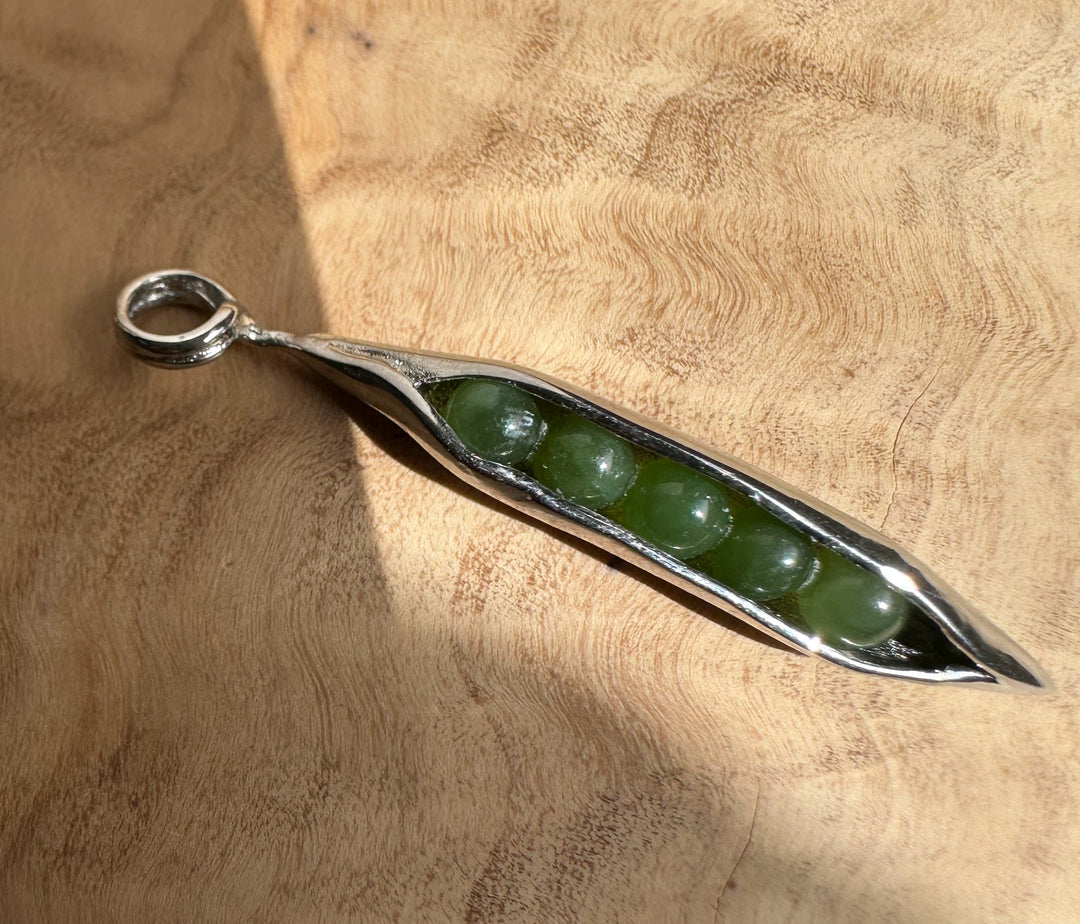 Five green jade beads inside a polished stainless steel peapod pendant hanging from a chain
