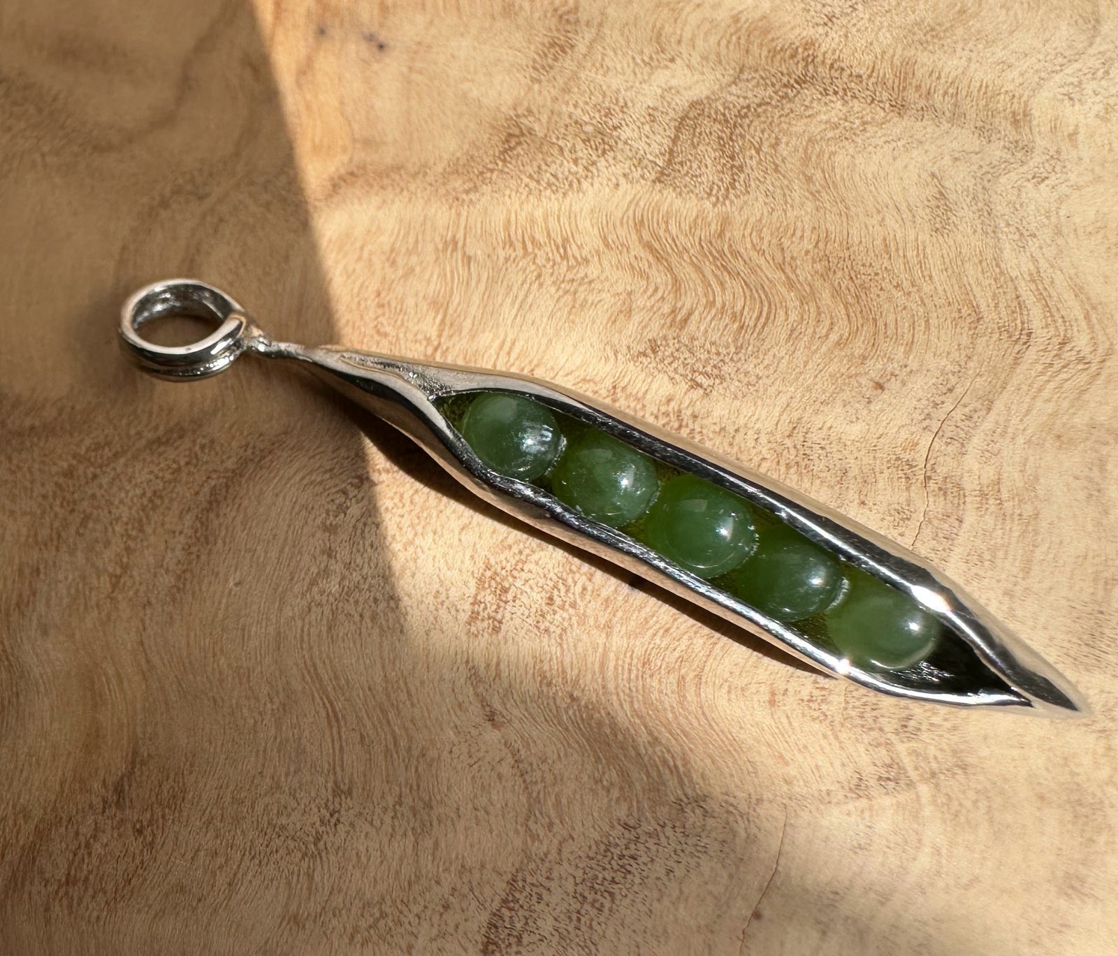 Five green jade beads inside a polished stainless steel peapod pendant hanging from a chain