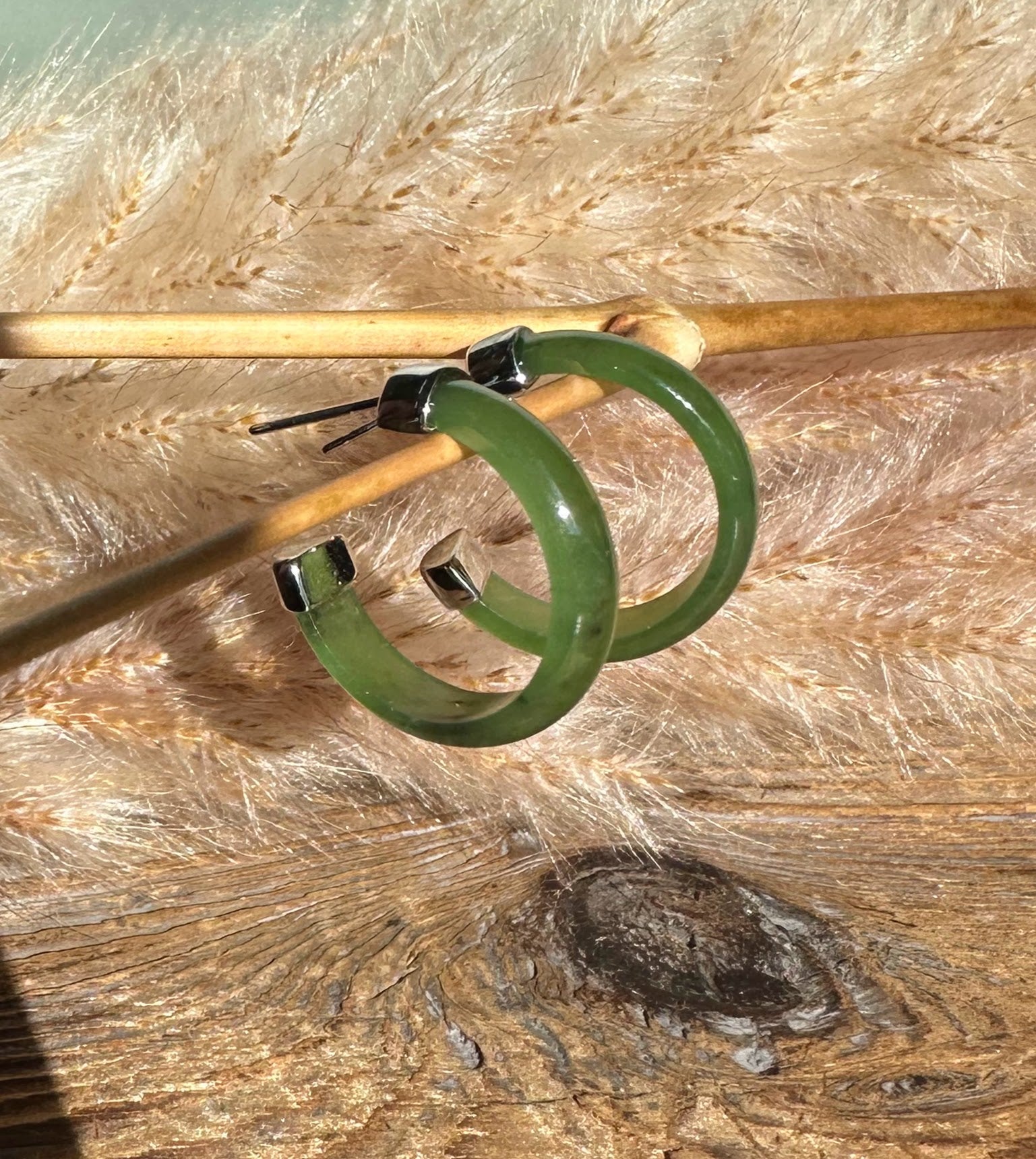 Green jade hoop earrings with stainless steel end caps resting on a wooden surface.