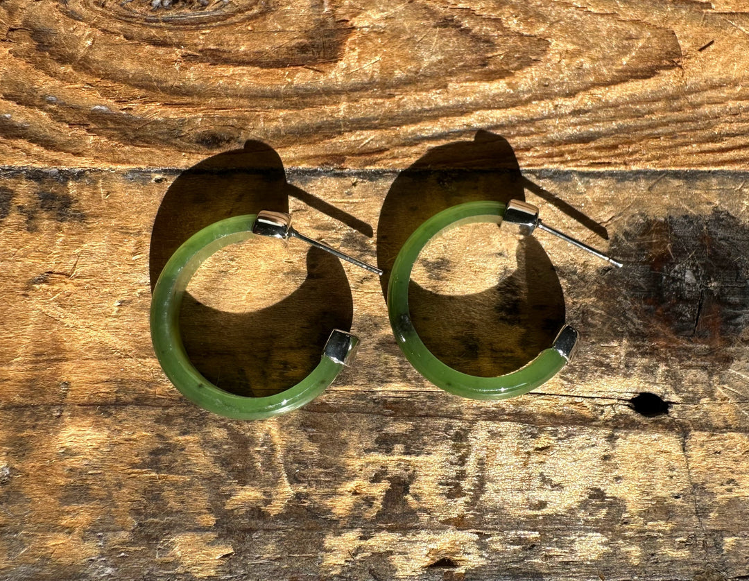 Pair of green Canadian Jade hoop earrings with silver ends laid on textured wood