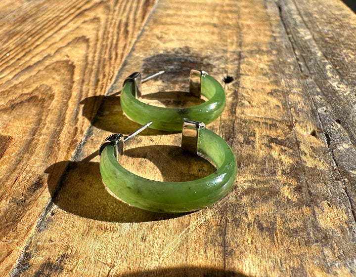 Green Canadian jade hoop earrings with stainless steel posts on a wooden surface