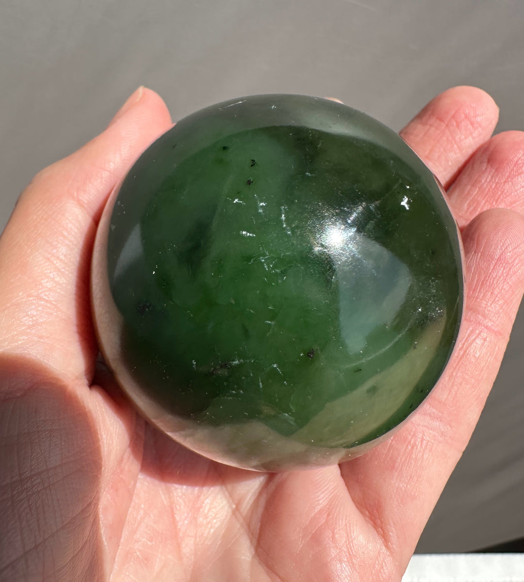 Hand holding a green stone sphere against a neutral background