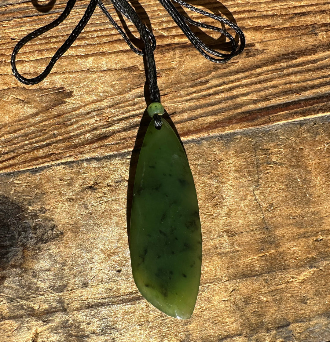 Green jade teardrop pendant on black cord with a small bead above against a wood background