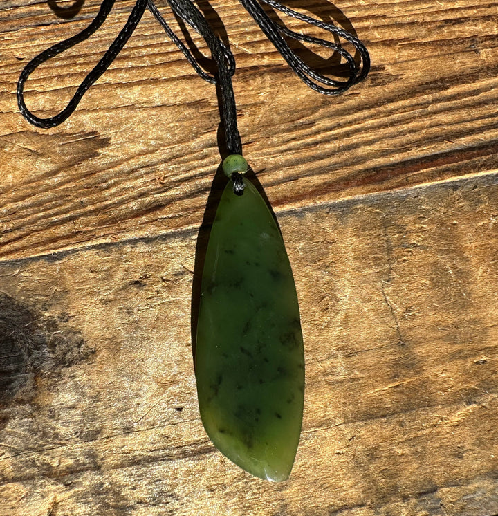 Green jade teardrop pendant on black cord with a small bead above against a wood background