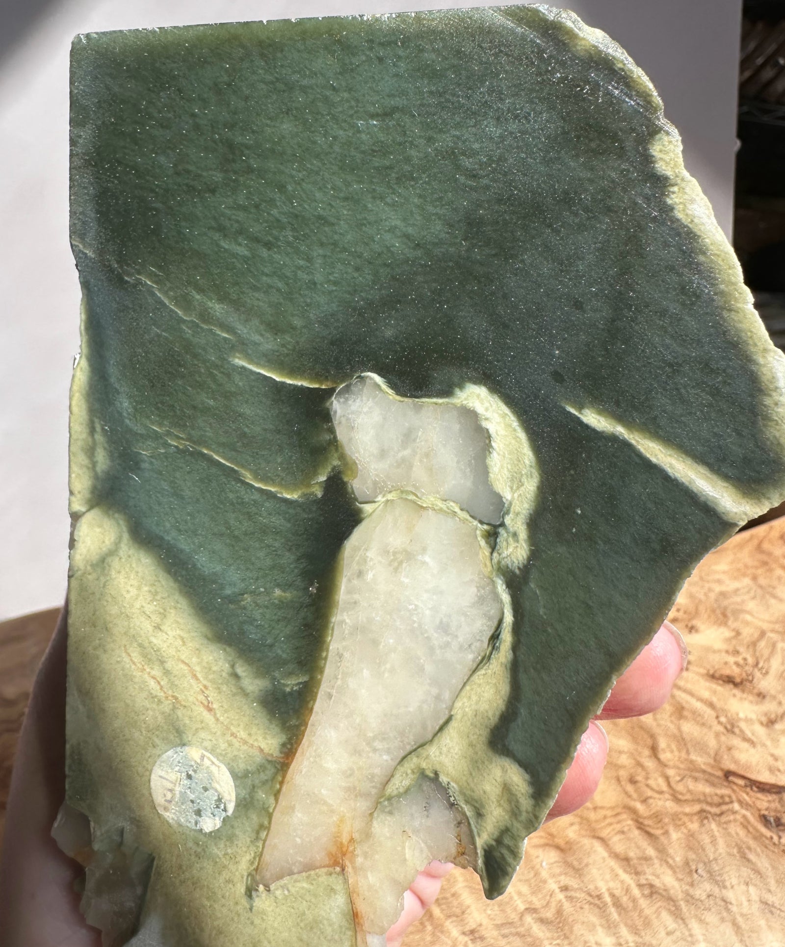Green jade with a small white quartz embedded inside, held by a hand.