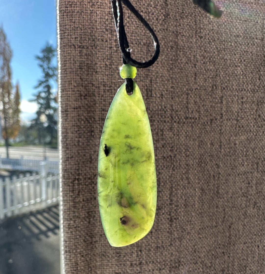 Close-up of lime green jade drop pendant on a black cord with bead outdoors