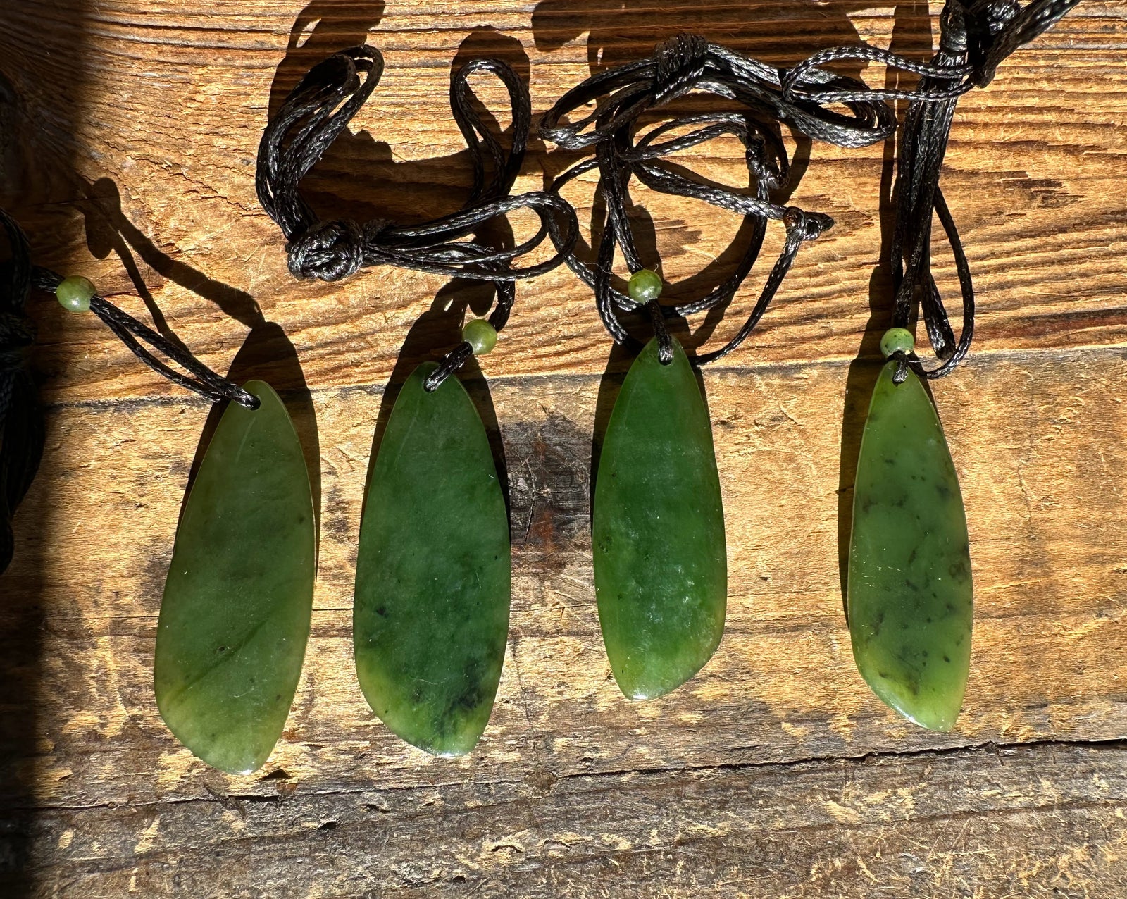 Four lime green jade drop pendants on black cords laid out on weathered wood