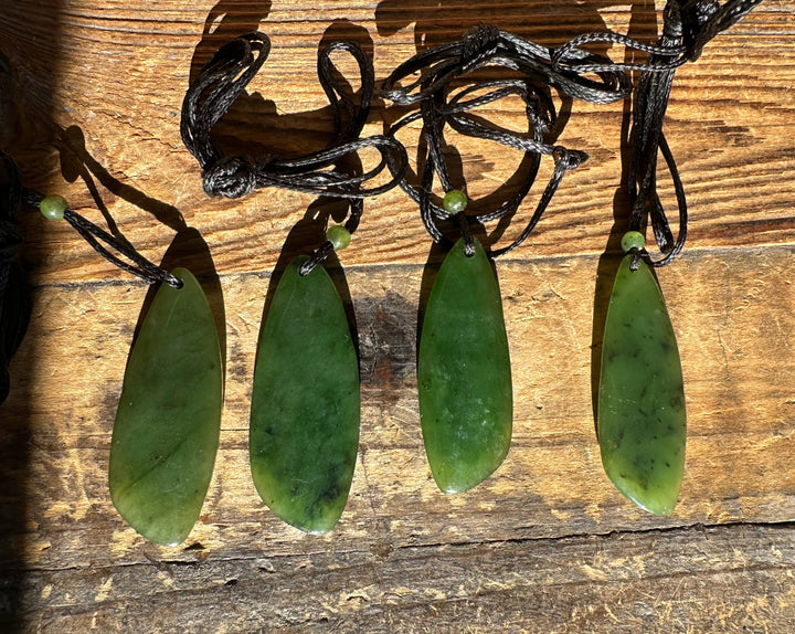 Four lime green jade drop pendants on black cords laid out on weathered wood
