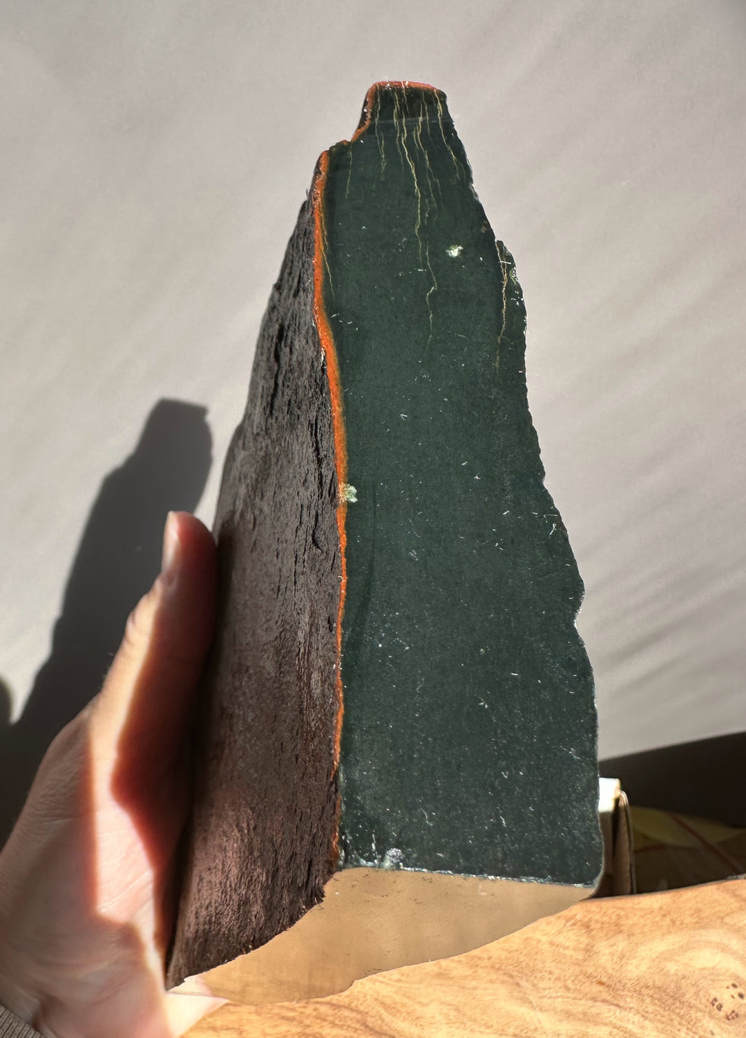 Person holding a dark green jade with a brownish red edge against a neutral background