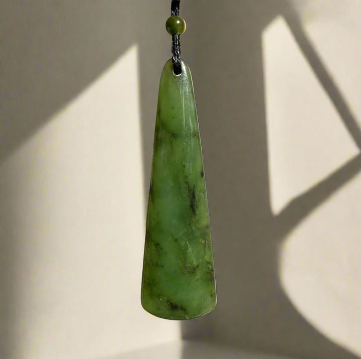 Single elongated green jade pendant on a black cord with a small green bead at the top