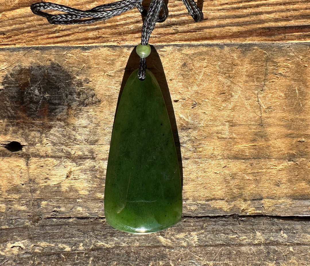 Dark green teardrop jade pendant on a black cord against a rustic wooden background