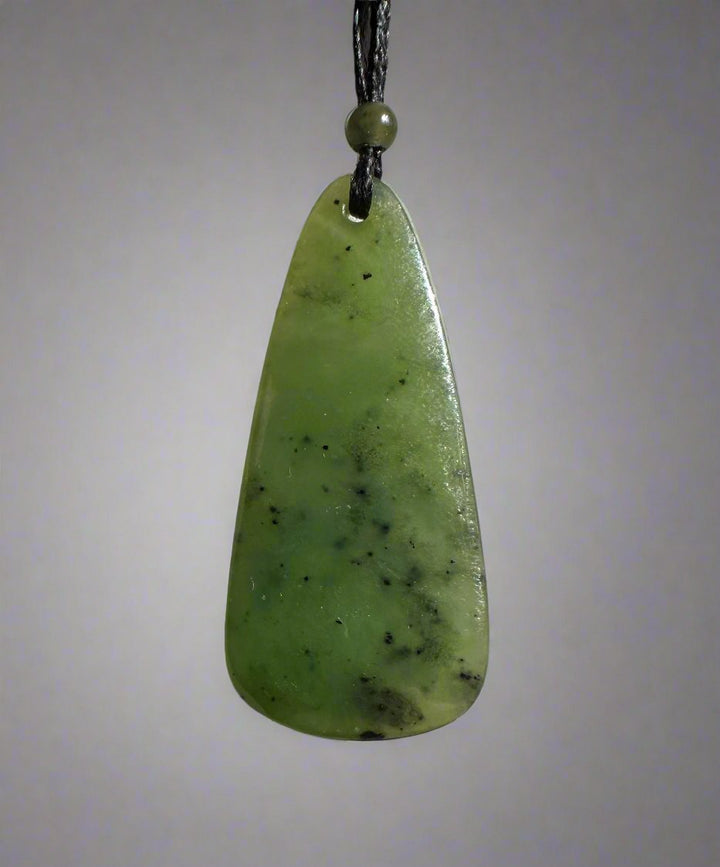 Light green jade teardrop pendant on black cord with a small bead, set against a pale grey backdrop