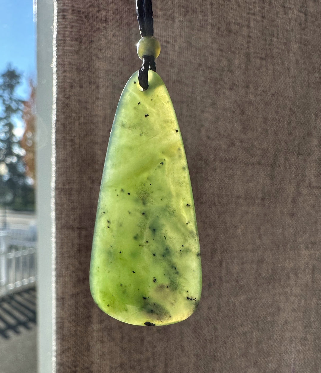 Pale lime green teardrop pendant with tiny black specks on a black cord