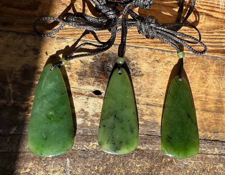 Three green jade teardrop pendants on black cords arranged on a rustic wooden surface