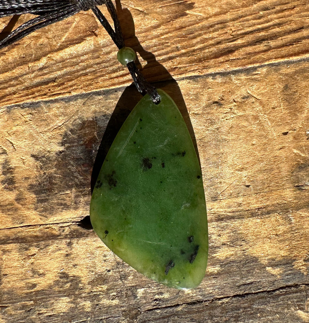 Close-up of the green jade pendant on a black cord resting on wood, showing darker green spots.