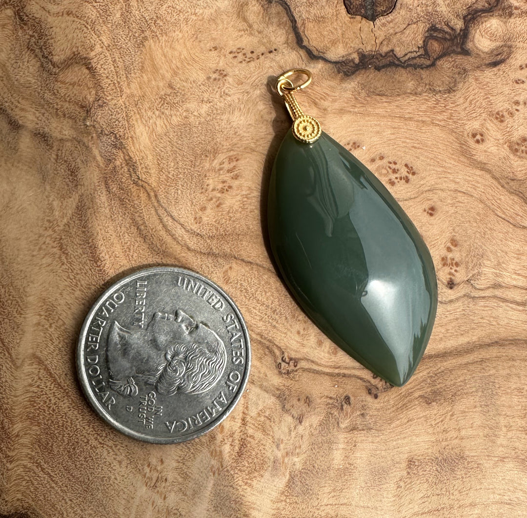 Green teardrop pendant next to a U.S. quarter on a wooden surface