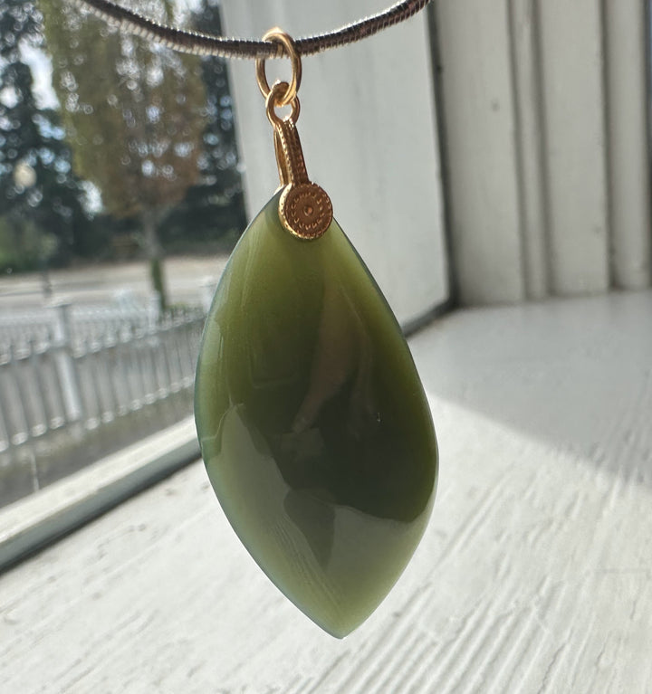 Green teardrop pendant on a chain with a blurred outdoor background