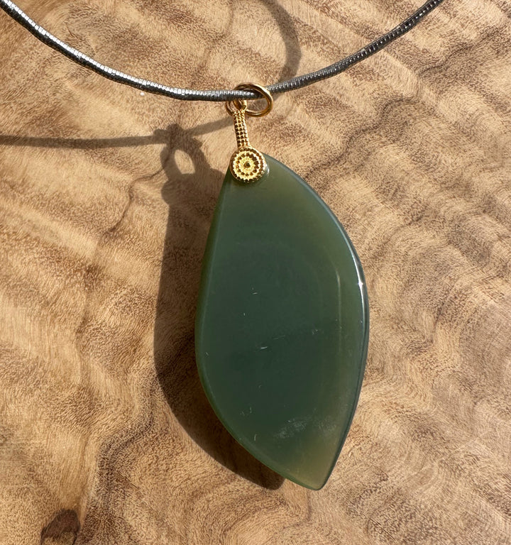 Green teardrop pendant on a black cord against a beige stone background