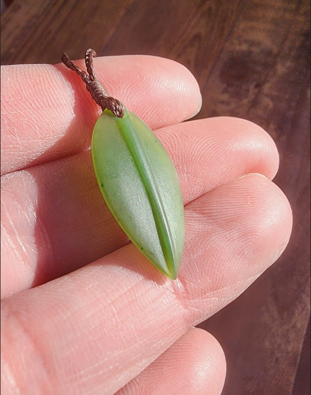Close up of a green jade leaf pendant held between fingers.