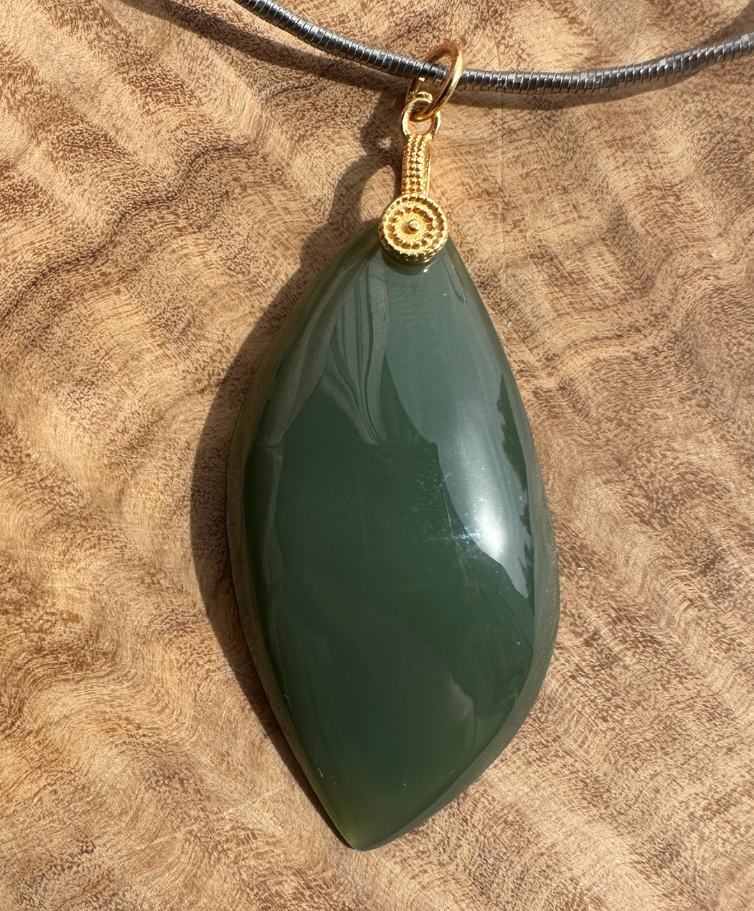 Green teardrop pendant on a gold chain against a brown textured background