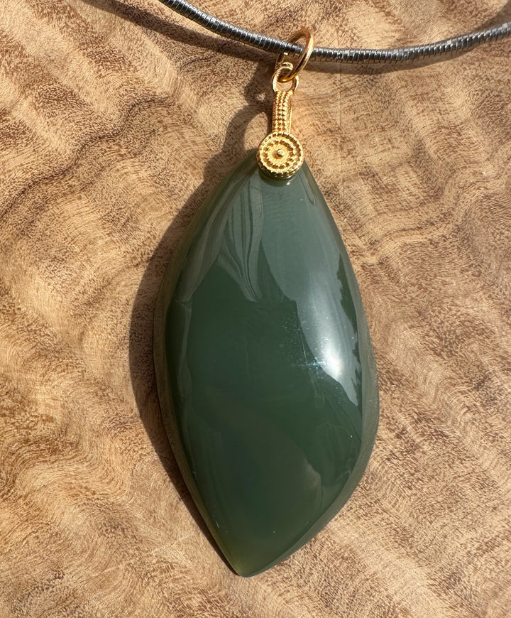 Green teardrop pendant on a gold chain against a brown textured background