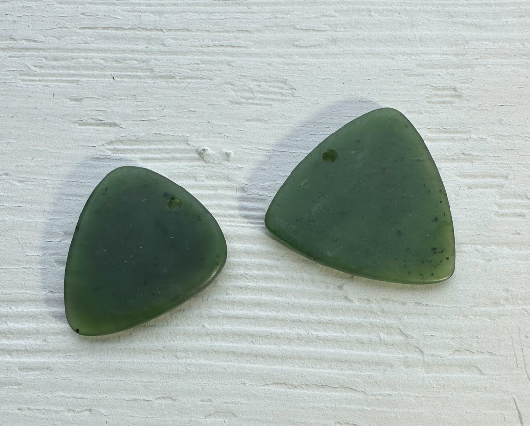 Two green jade guitar picks resting on a light textured surface.