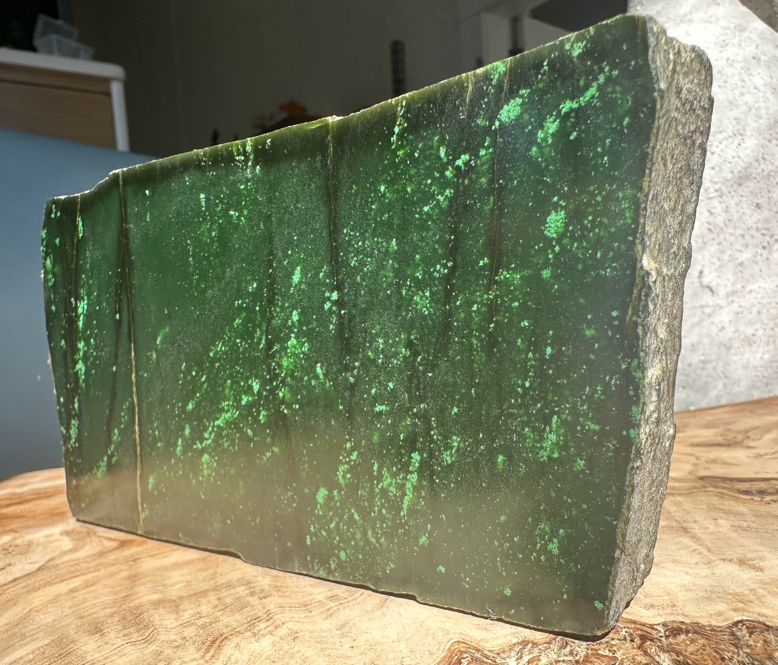 Side view of Cassiar jade rough block with bright green specks and a rough natural edge