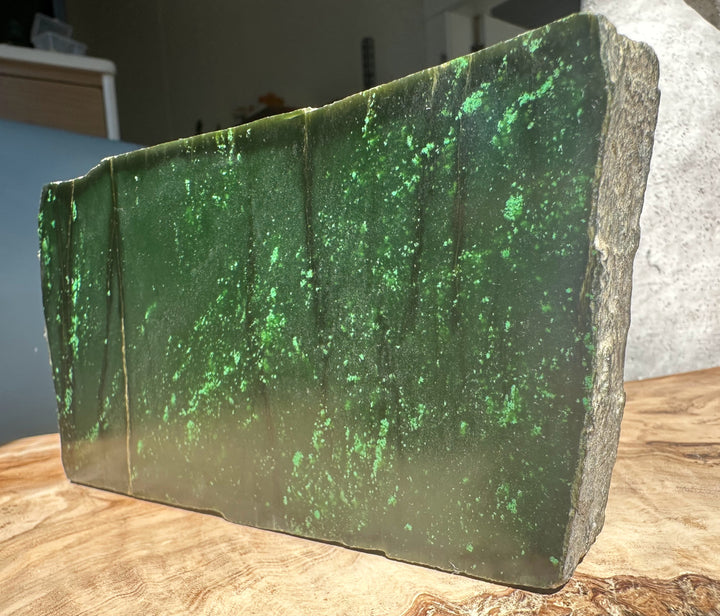 Side view of Cassiar jade rough block with bright green specks and a rough natural edge