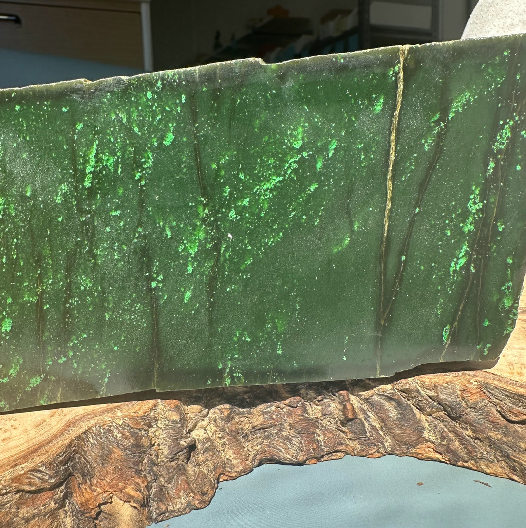 Cassiar Jade rough slab with deep green surface and bright green speckles resting on a wooden display base.